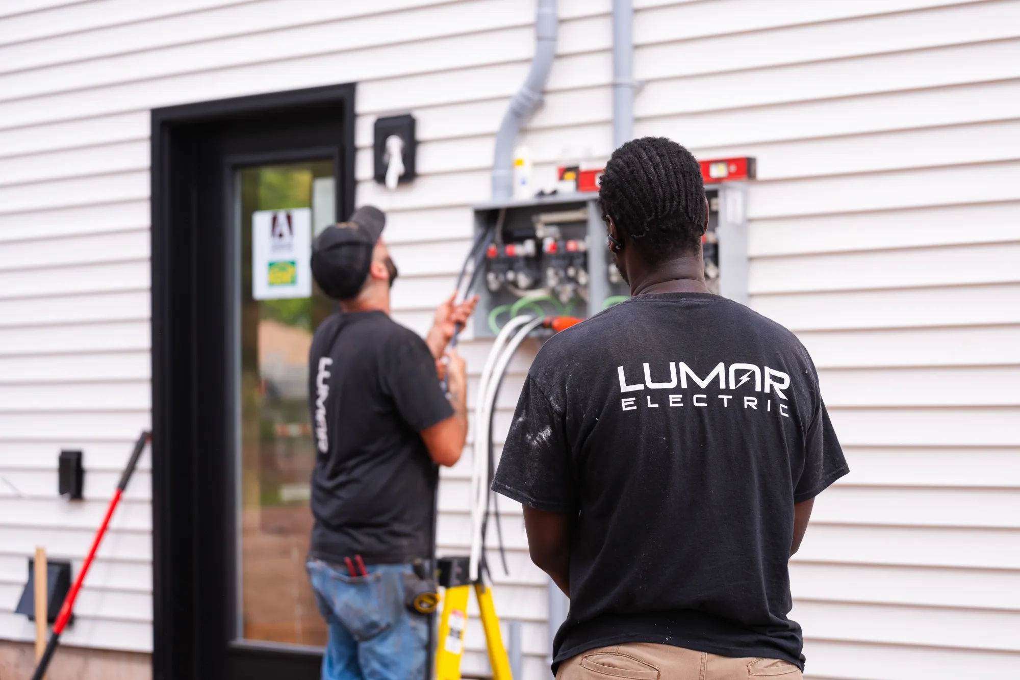 Two LuMar Electric electricians at an exterior service panel