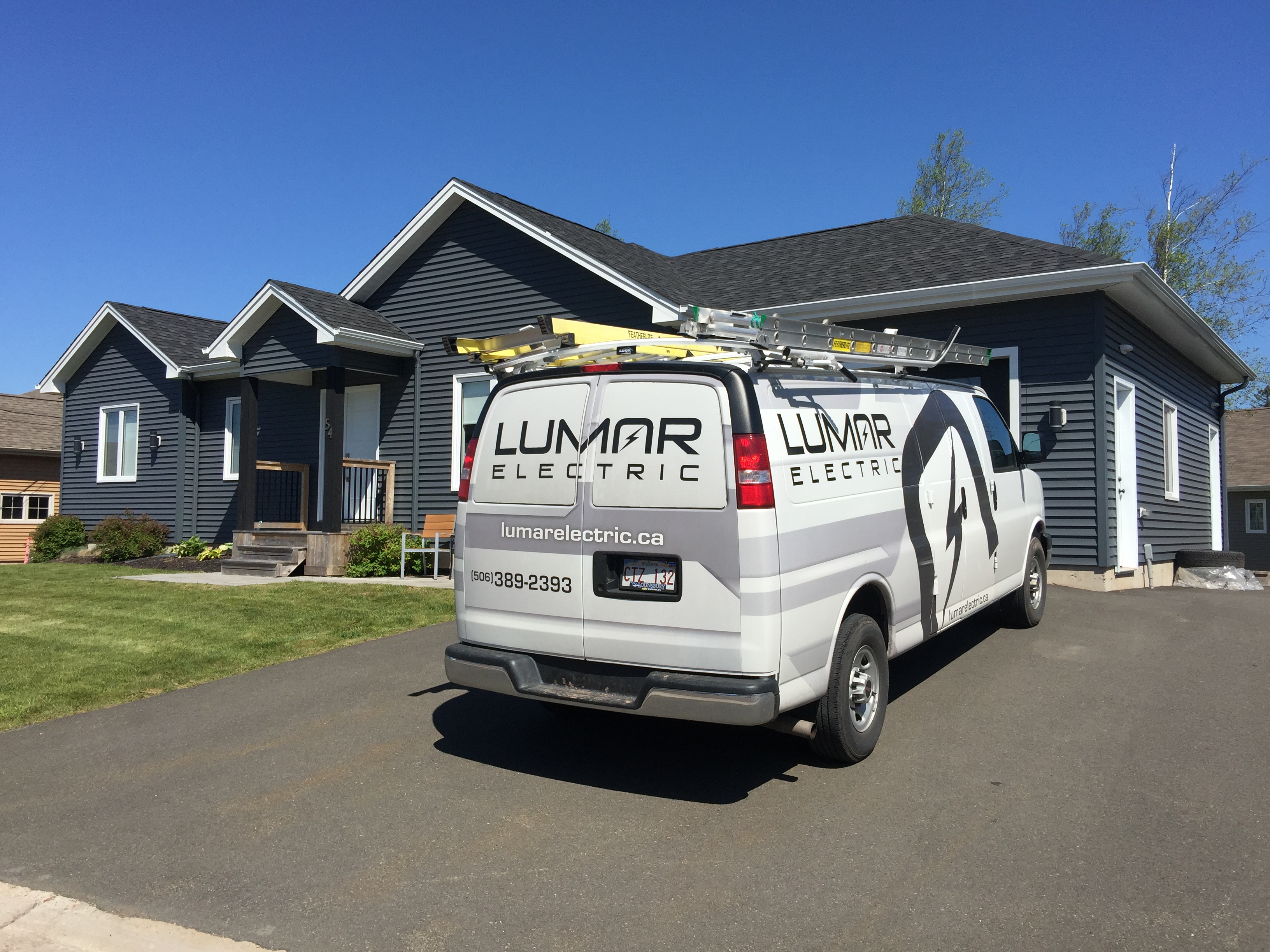 Des camionnettes de service LuMar Electric stationn&eacute;es devant une rang&eacute;e de maisons