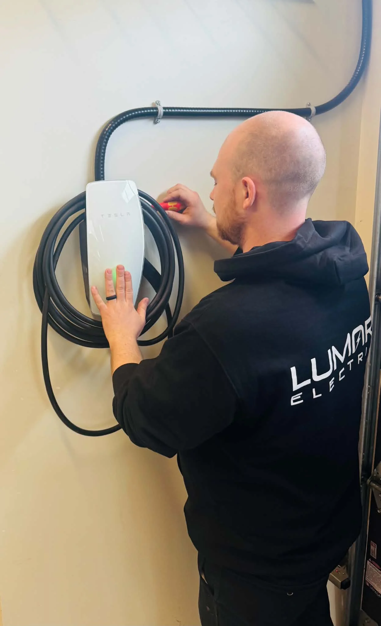 A LuMar Electric electrician fitting a Tesla Wall Connector in a garage